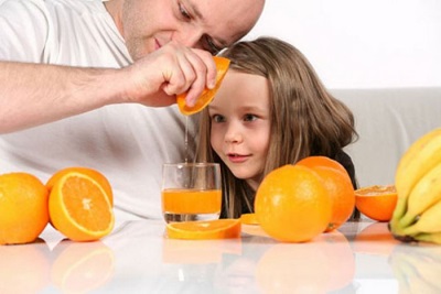 Fresh juice from orange is prepared by a child with dad