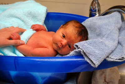 Baby in 1 month bathes in the bath in the arms of the mother